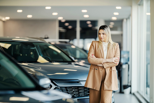 A female car seller is walking around car dealership salon and looking at the cars.